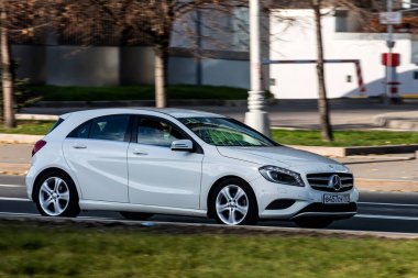 Moskova; Rusya - 14 Ekim 2021: Beyaz Mercedes-Benz A sınıfı sıcak bir sonbahar gününde bir parkın arka planına doğru hızla ilerliyor.