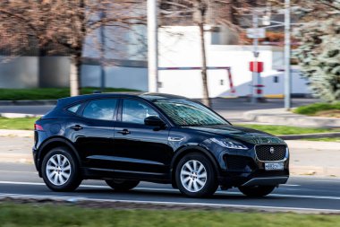 Moskova; Rusya - 14 Ekim 2021: Siyah Jaguar E-PACE sıcak bir sonbahar gününde bir parkın arka planına doğru hızla sürüyor