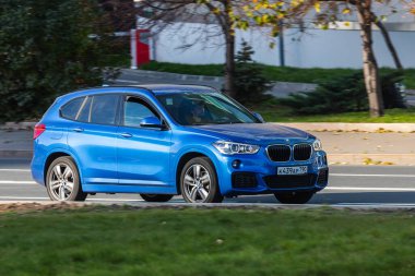 Moskova; Rusya - 14 Ekim 2021: Mavi BMW X3 sıcak bir sonbahar gününde bir parkın arka planına doğru hızla ilerliyor