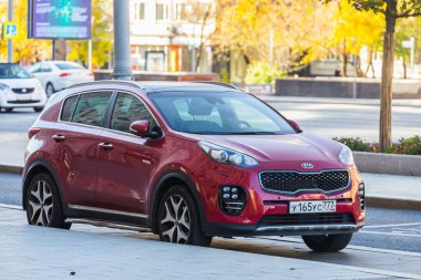 Moskova, Rusya - 13 Ekim 2021: Kırmızı Kia Sportage sıcak bir sonbahar gününde bir binanın ve ağaçların arkasına park edilmiştir.