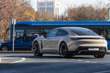 Moskova; Rusya - 13 Ekim 2021: Gri Porsche Taycan turbo, sıcak bir sonbahar gününde bir parkın arka planına doğru hızla sürüyor