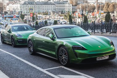 Moskova, Rusya - 13 Ekim 2021: 2 yeşil Porsche Taycan ve 911 sıcak bir sonbahar gününde bir binanın arka planına karşı sokağa park edildi