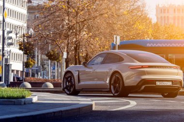 Moskova; Rusya - 13 Ekim 2021: Gri Porsche Taycan turbo, sıcak bir sonbahar gününde bir parkın arka planına doğru hızla sürüyor