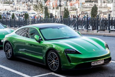 Moskova, Rusya - 13 Ekim 2021: Yeşil Porsche Taycan sıcak bir sonbahar gününde bir binanın arka planına park etti