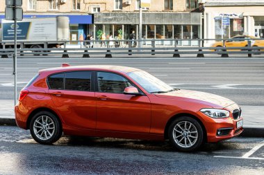 Moskova; Rusya - 15 Ekim 2021: Kırmızı BMW 1 serisi sıcak bir sonbahar gününde bir caddenin arka planına park edilmiştir.
