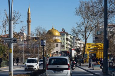 Manavgat, Türkiye - 20 Ocak 2022: Farklı alçak binalar, nehir üzerinde sarı köprü ve cami, faal araba trafiği, dükkanları olan şehir caddesi