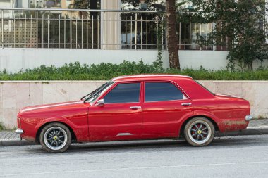 Yan, Türkiye - 18 Ocak 2022: Klasik kırmızı Ford Taunus i sıcak bir yaz gününde bir binanın, ağaçların, dükkanların zeminine karşı sokağa park edilmiştir.
