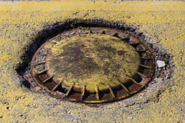 Yerdeki paslı rögar deliğinin yakın çekim demir görüntüsü.