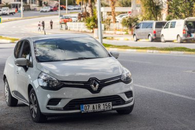 Yana, Türkiye - 19 Ocak 2022: Beyaz Renault Clio, sıcak bir yaz gününde bir binanın, ağaçların, dükkanların zeminine park etti.