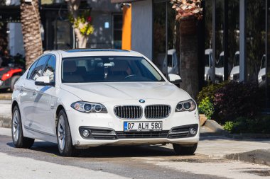 Yana, Türkiye - 23 Ocak 2022: Beyaz BMW 5 serisi sıcak bir günde bir binanın, ağaçların, otelin zeminine park edilmiştir.