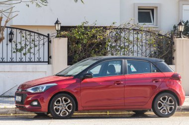 Yana, Türkiye - 22 Ocak 2022: Kırmızı Hyundai i20, sıcak bir günde bir binanın arka planına, ağaçlara park edilmiştir.