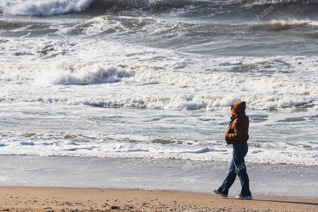 The woman walks along the beach and looks at the restless deep sea. Feeling calm, cool, relaxed.