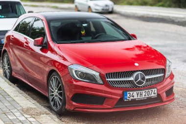 Yan, Türkiye - 25 Ocak 2022: Kırmızı Mercedes-Benz A sınıfı, sıcak bir yaz gününde yola ve ağaçlara karşı park halinde.