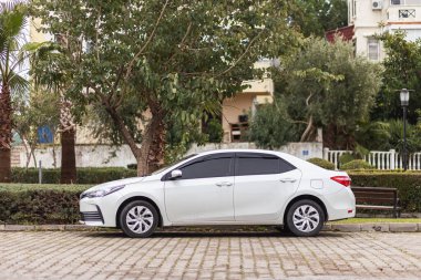 Yan, Türkiye - 25 Ocak 2022: Beyaz Toyota Corolla, sıcak bir yaz gününde parka karşı park halinde.
