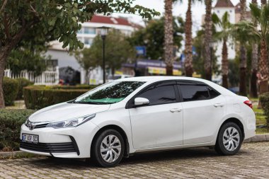 Yan, Türkiye - 25 Ocak 2022: Beyaz Toyota Corolla, sıcak bir yaz gününde parka karşı park halinde.