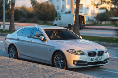 Yana, Türkiye - 27 Ocak 2022: Beyaz BMW 5 serisi bir binanın, dükkanın arka planına karşı gün batımına park ediyor