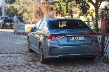 Yana, Türkiye - 27 Ocak 2022: Gümüş rengi Toyota Corolla sıcak bir yaz gününde bir bina, çit, dükkan zeminine karşı sokağa park edilmiştir.
