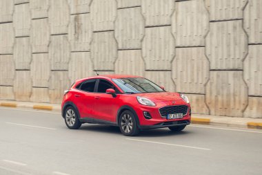 Yana, Türkiye - 27 Ocak 2022: Kırmızı Ford Puma bir yaz gününde taştan bir duvarın önünde araba sürüyor.