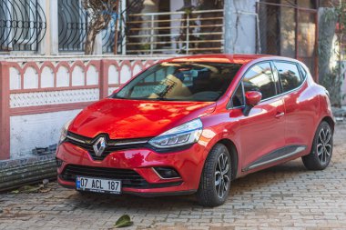 Yana, Türkiye - 27 Ocak 2022: Kırmızı Renault Clio sıcak bir yaz gününde bir bina, çit, dükkan zeminine karşı sokağa park edilmiştir.