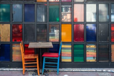 Atmosferik yaz fotoğrafçılığı. Masadaki tahta kafe sandalyeleri çok renkli bardakların arka planına karşı. Açık sokak kafesi