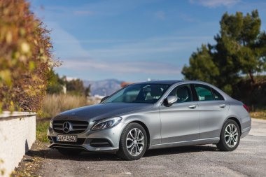 Yana, Türkiye - 28 Ocak 2022: Gümüş Mercedes-Benz C sınıfı sıcak bir günde bir binanın zeminine, ağaçlara karşı sokağa park edilmiştir.