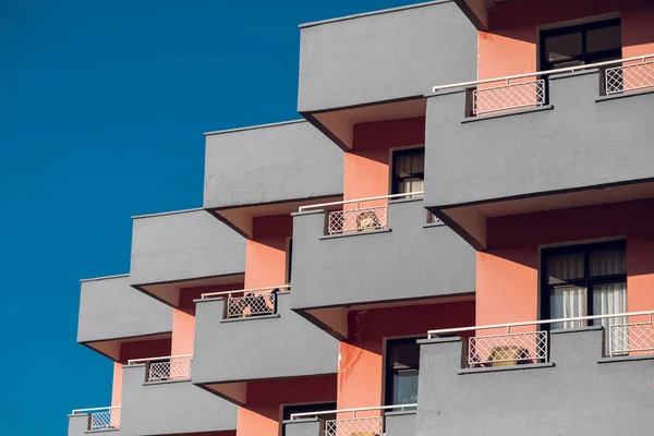 A pink residential building with flat, identical balconies with ripped air conditioners . Balcony pattern