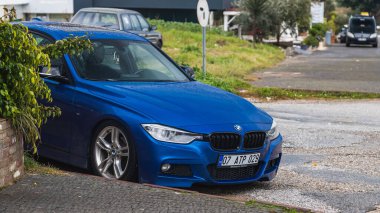 Yana, Türkiye - 30 Ocak 2022: Mavi BMW 3 serisi sıcak bir günde yolun arka planına, parka park edildi