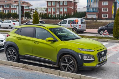 Yan; Türkiye 01 Şubat 2022: Yeşil Hyundai Kona, sıcak bir yaz gününde bir binanın arka planına, şehir trafiğine park etti 