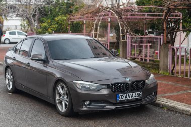 Taraf; Türkiye 01 Şubat 2022: Kahverengi BMW 3 serisi f30 park halindedir; sıcak bir sokakta; bir bahçe zeminine karşı gün 