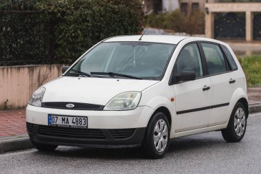 Taraf, Türkiye - 2 Şubat 2022: Beyaz Ford Fiesta sıcak bir günde bir binanın, parkın, çitin zeminine park etti.