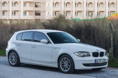 Yan, Türkiye 2 Şubat 2022: Beyaz BMW 1 serisi sıcak bir sonbahar gününde bir caddenin arka planına park edildi 