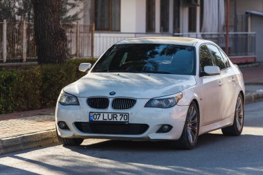 ; Türkiye 6 Şubat 2022: Beyaz BMW 5 serisi bir binanın, ağaçların önünde gün batımına park ediyor 