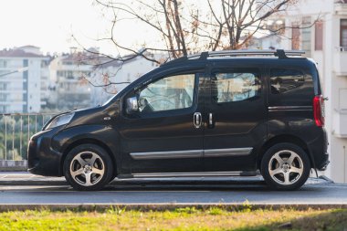 Yan; Türkiye 06 Şubat 2022: Siyah Fiat Fiorino bir yaz günü bir şehrin arka planına karşı sokağa park ediyor 
