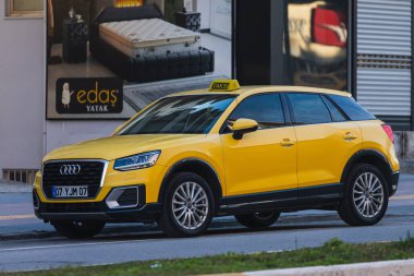 ; Türkiye 6 Şubat 2022: Sarı taksi Audi Q2 sıcak bir yaz gününde bir dükkanın arka planına doğru hızla ilerliyor 