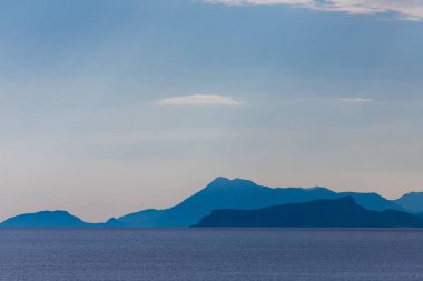 Yüksek dağların panoramik manzarası, karla kaplı tepeler bulutlu mavi bir gökyüzüne karşı.