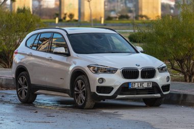 Yan, Türkiye 13 Şubat 2022: Beyaz BMW X1 bir yaz günü bir parkın arka planına karşı sokağa park ediyor 
