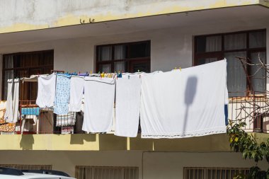 Bir ipe yakın çekim, yeni yıkanmış beyaz çarşaflar, bir havlu, kuaför gömlekleri ve diğer şeyler asılmış.