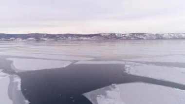 Dondurucu Baykal. Baykal kış uykusuna yatar. Baikalsk şehrinin buzlu kıyıları ve dağların manzarası. Doğal arka plan. Mevsimleri değiştiriyorum. Bir İHA 'dan ateş etmek.
