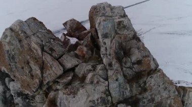 Donmuş Baykal Gölü. Kışın Olkhon Adası. Meşhur Şamanka kayasının panoramik manzarası tepede eski bir karaçam ağacı ve buzun üzerinde seyahat eden turistler. İnsansız hava aracından kış ateşi.