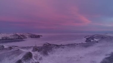 Northern landscape of frozen lake drone flying down with beautiful reflection on ice at sunset. Amazing winter Baikal with a red sunrise. Watch a drone fly on the northern ice lake. Natural reflection