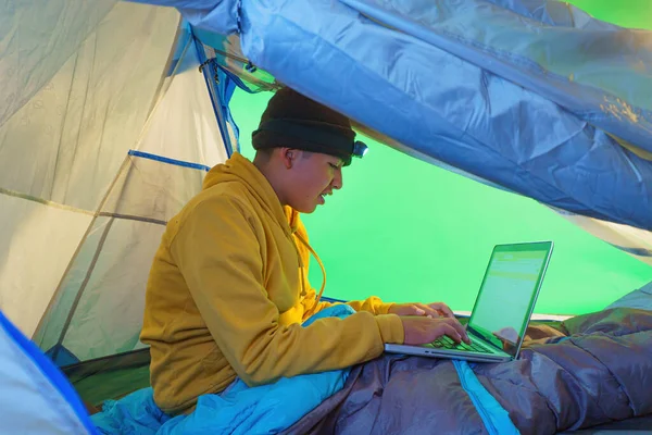 a boy playing with a laptop inside a tent on a green background