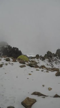  tent standalone among rocks on the top of the mountain surrounded with mountains and clouds