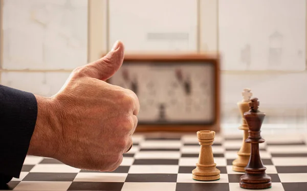 Hand en schaakbord met figuren en klok op wazig venster achtergrond — Stockfoto