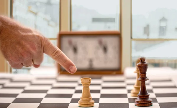 Hand en schaakbord met figuren en klok op wazig venster achtergrond — Stockfoto