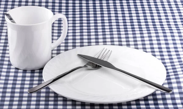 Caneca Empy com colher, prato com uma faca e garfo na toalha de mesa em uma gaiola. Vista de cima com espaço de cópia — Fotografia de Stock