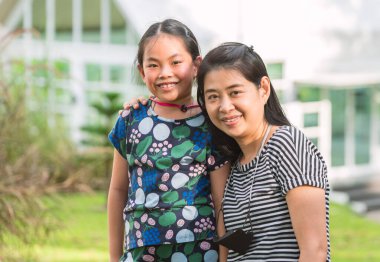 Annesi ile birlikte Asyalı bir çocuğun Tayland 'da bir tatil köyünde portresi. İkisinin de boynunda yüz maskesi var. Gülümseyen yüz, kameraya bakan gözler..