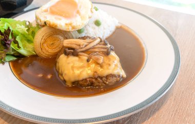 Japon Pork Burger menüsü, Japon Burger 'ini kapat ve üzerine peynir, Shimeji mantarı ve kızarmış yumurta konmuş körili pilav. Beyaz yuvarlak tabakta taze salata..