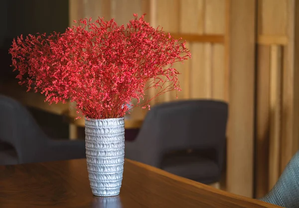 Beautiful silver vase with sand texture and red-colour plant in wooden table of sharing work space in a building, blank space for text.