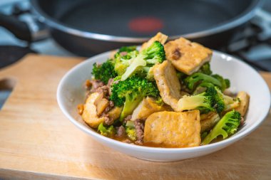 Karıştırılmış Brokoli ve kızarmış tofu, sağlıklı Asya ev yapımı menü, beyaz tabakta yemek bir mutfakta ahşap kesme tahtasının üzerinde, yiyecekleri kapat, doğal ışıklandırma görüntüsü..
