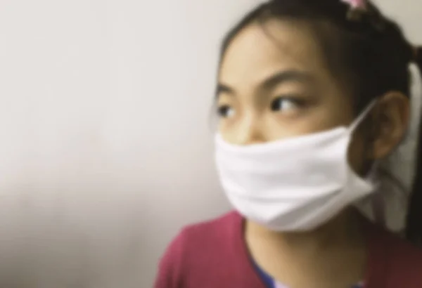 Close-up and blurred image portrait of an Asian child girl wears white facemask, looks aside to the light from outside, blurred image of child girl with facemask.